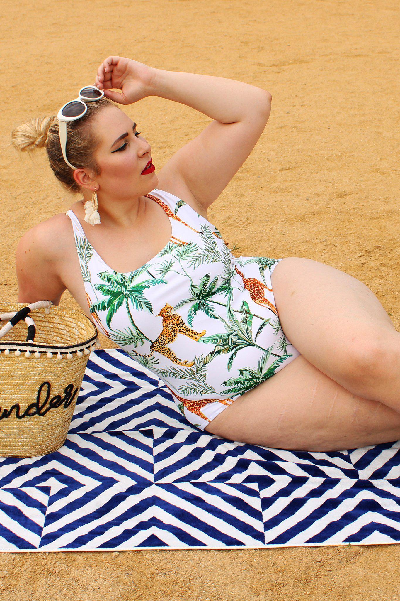 Model posing on towel wearing plus-size jungle print one-piece swimsuit